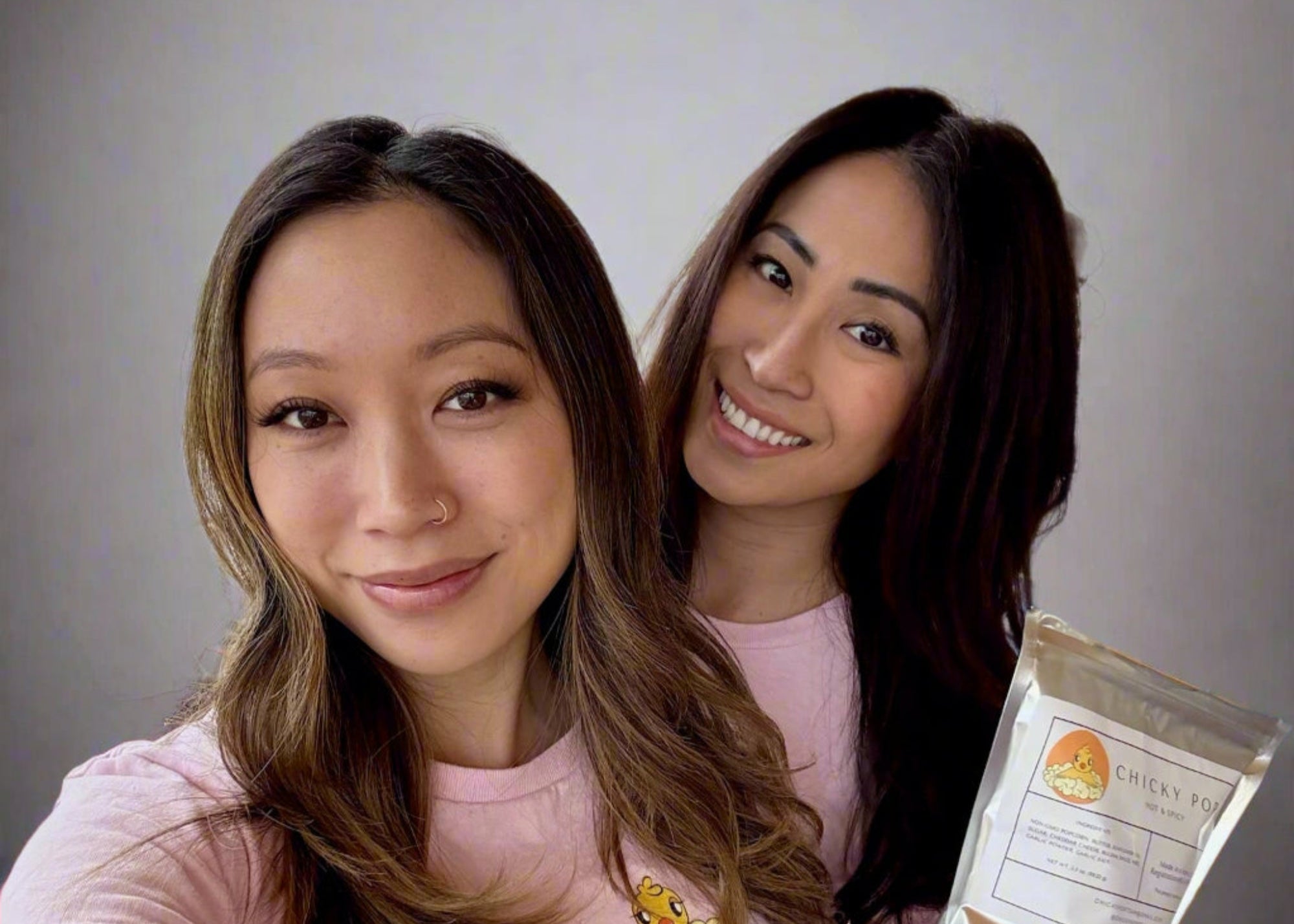 Two women in pink shirts with a snack package in front of a large window.